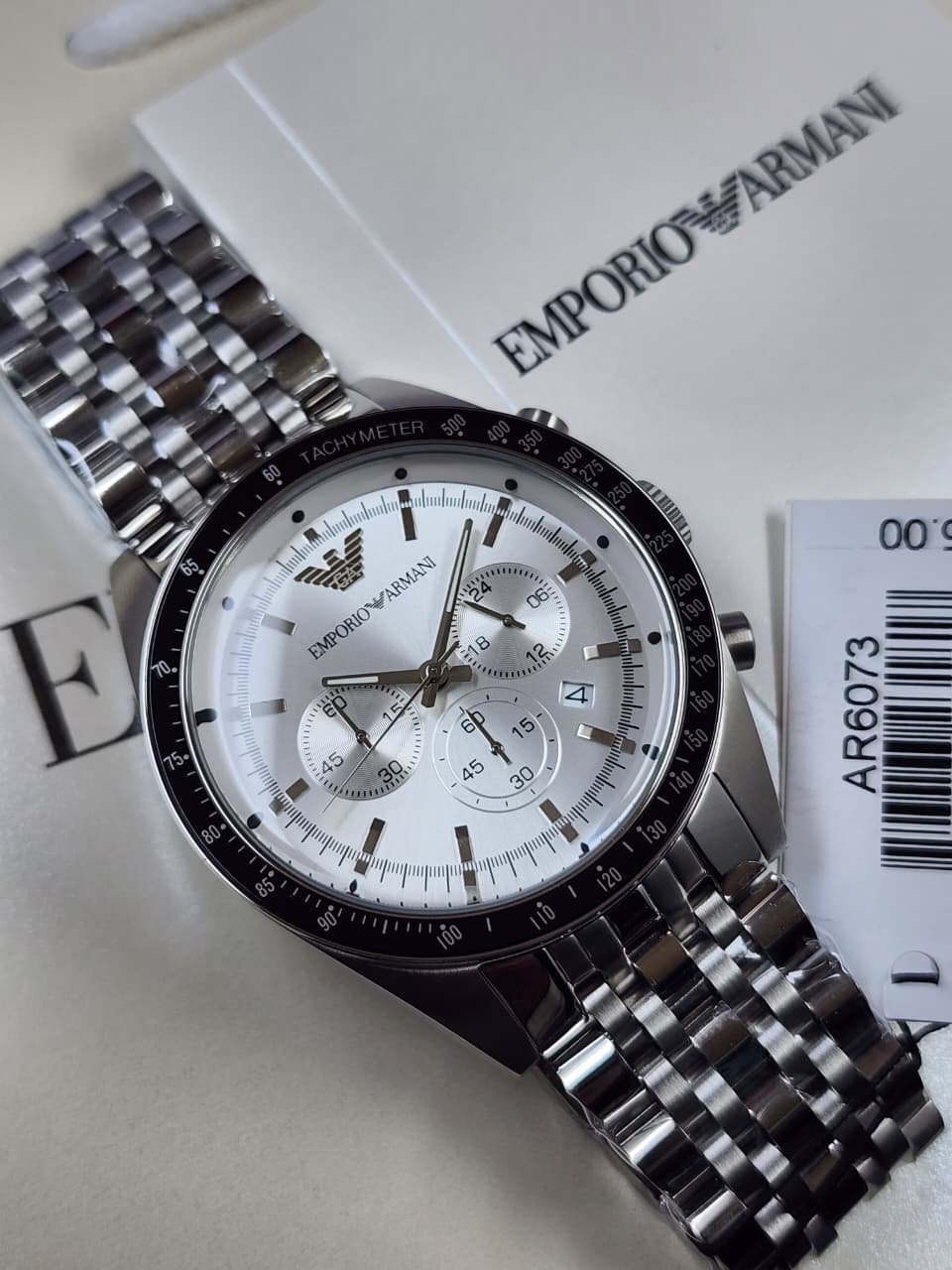 Silver Emporio Armani watch on a white background with brand packaging.